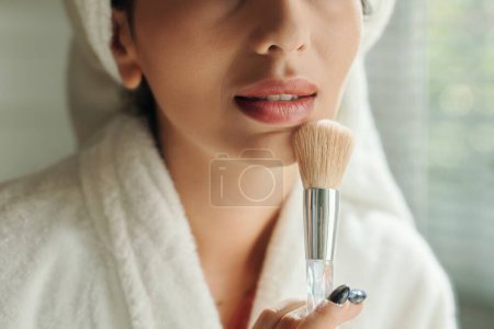Téléchargez les photos : Jeune femme appliquant de la poudre sur son menton pour fixer le maquillage - en image libre de droit