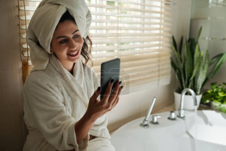 Photo for Smiling woman video calling best friend after taking shower - Royalty Free Image