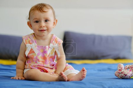 Photo for Portrait of cute adorable little girl sitting on bed and smiling at camera - Royalty Free Image
