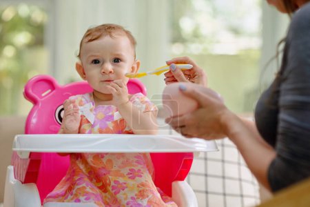 Foto de Retrato de niña sentada en la silla de alimentación cuando la madre le da comida en puré - Imagen libre de derechos