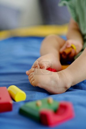 Photo for Feet of little baby playing with wooden toys on bed - Royalty Free Image