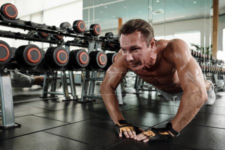 Photo for Fit mature man doing diamond push-ups on gym floor - Royalty Free Image