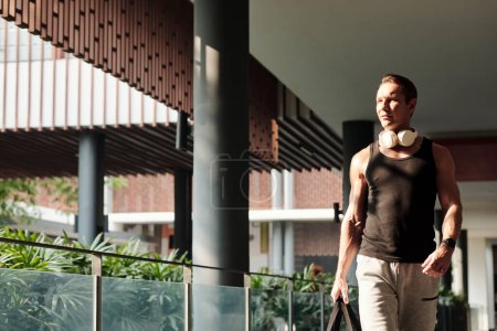 Foto de Retrato de deportista determinado con auriculares y bolso caminando al gimnasio por la mañana - Imagen libre de derechos