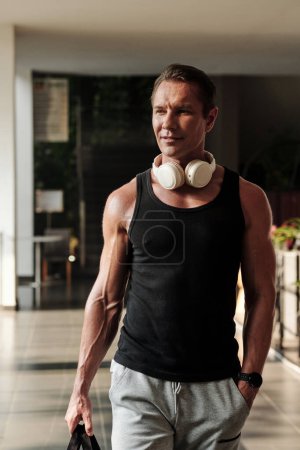 Téléchargez les photos : Fit homme mature positif avec écouteurs se précipitant à la salle de gym le matin - en image libre de droit