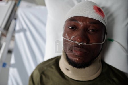 Foto de Vista de ángulo alto del soldado herido afroamericano mirando a la cámara mientras está acostado en el hospital militar - Imagen libre de derechos