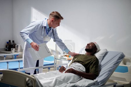 Foto de Médico preguntando acerca de la condición de salud al soldado mientras yacía en la cama en la sala - Imagen libre de derechos