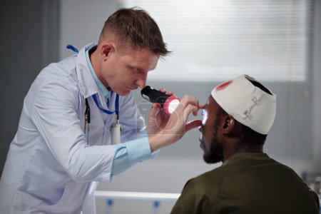 Foto de Médico profesional en bata blanca examinando soldado lesionado durante el examen médico en el hospital - Imagen libre de derechos