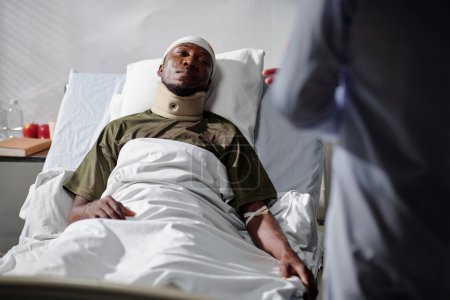 Foto de Soldado afroamericano con lesión acostado en la cama en el hospital y escuchando al médico - Imagen libre de derechos