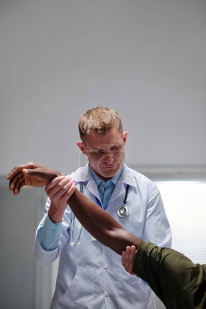 Téléchargez les photos : Image verticale du médecin professionnel examinant le bras du patient à l'hôpital - en image libre de droit