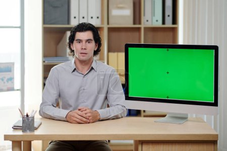 Téléchargez les photos : Courtier masculin sérieux et confiant ou PDG faisant la présentation tout en étant assis sur le lieu de travail avec écran d'ordinateur avec écran vert - en image libre de droit