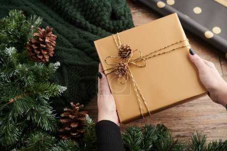 Téléchargez les photos : Mains de femme décorant des cadeaux de Nouvel An avec du papier doré et des cônes de pin - en image libre de droit