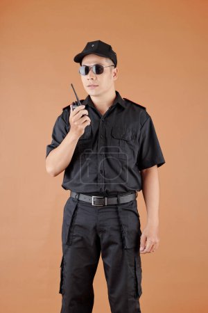 Photo for Portrait of male security guard in sunglasses talking on walkie-talkie with coworker - Royalty Free Image