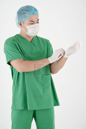 Foto de Cirujano serio en máscara protectora ponerse guantes de goma antes de la cirugía - Imagen libre de derechos