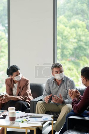 Photo for Business people in protective masks meeting to discuss company development and anti-crisis management strategy - Royalty Free Image