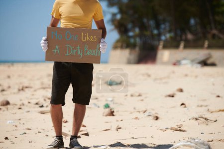 Téléchargez les photos : Image recadrée d'un volontaire tenant personne n'aime une pancarte sale sur la plage - en image libre de droit