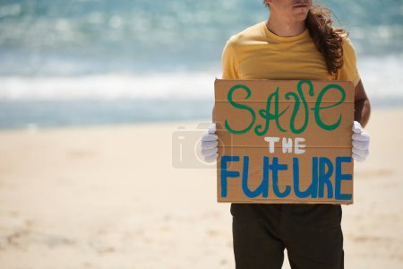 Photo for Cropped image on volunteer standing on sandy beach and holding save the future placard - Royalty Free Image