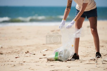 Zugeschnittenes Bild einer freiwilligen Helferin, die Müll, Plastik- und Glasflaschen beim Aufräumen am Strand aufsammelt. Tag der Erde