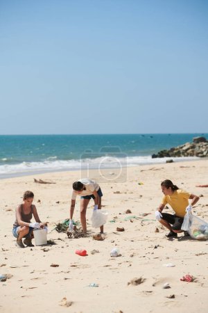 Photo for Group of volunteers picking up plastic trash in bags when cleaning sandy beach on Earth day - Royalty Free Image