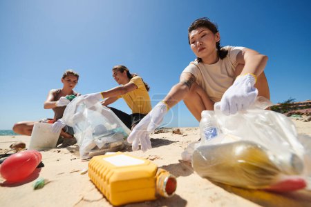 Foto de Grupo de amigos voluntarios en la playa del mar y recogiendo basura para limpiar la costa - Imagen libre de derechos