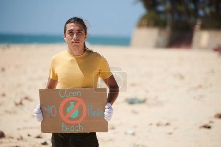 Photo for Portrait of serious young volunteer holding environmental poster clean beach - Royalty Free Image