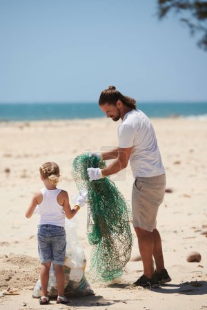 Padre e hija poniendo red de plástico derramada en la playa en una gran bolsa de plástico