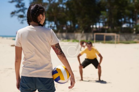 Téléchargez les photos : Vue arrière de la jeune femme debout avec balle de volley-ball, son petit ami est prêt à l'attraper - en image libre de droit