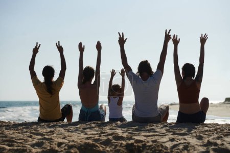 Téléchargez les photos : Deux couples et une petite fille assis sur la plage et levant les bras dans les airs, vue de dos - en image libre de droit
