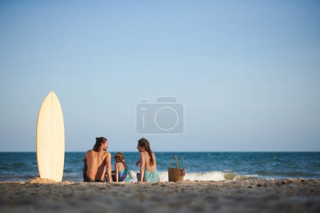 Foto de Los padres y la pequeña hija descansando en la playa del mar después de surfear - Imagen libre de derechos
