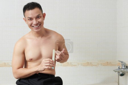 Téléchargez les photos : Portrait de happly jeune homme asiatique assis sur le bord de la baignoire et de limer les ongles - en image libre de droit