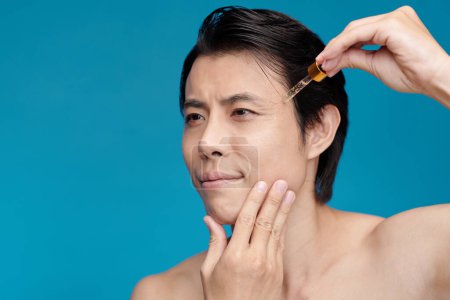 Foto de Hombre aplicando suero de vitamina C en la cara, aislado en azul - Imagen libre de derechos