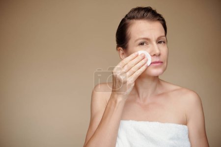 Téléchargez les photos : Femme mûre essuyant le maquillage avec un coton trempé dans de l'eau micelaire - en image libre de droit