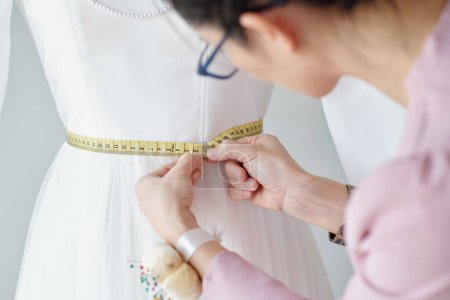 Photo for Seamstress double checking waist length of dress on mannequin - Royalty Free Image