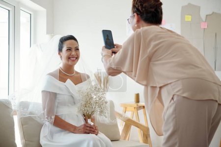 Téléchargez les photos : Mariée heureuse posant pour la photo lorsque la mère photographie sur smartphone - en image libre de droit