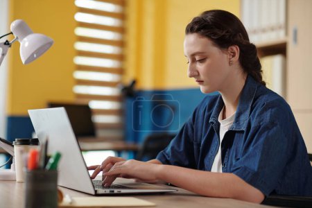 Foto de Mujer joven seria que trabaja en el ordenador portátil en la oficina - Imagen libre de derechos