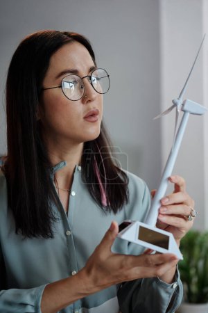 Foto de Retrato de una joven pensativa en gafas mirando el modelo de turbina de viento de plástico en sus manos - Imagen libre de derechos