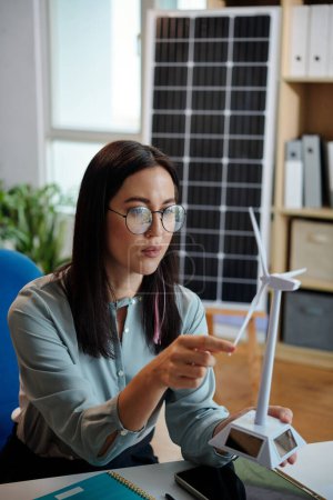 Photo for Serious female wind energy engineer looking at model of new wind turbine - Royalty Free Image
