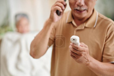 Téléchargez les photos : Homme âgé appelant une ambulance après avoir mesuré la température corporelle de sa femme - en image libre de droit