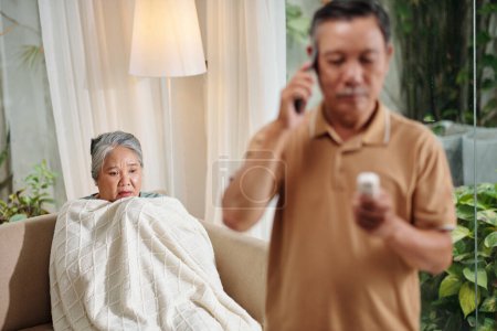 Photo for Sick senior woman sitting under warm blanket when husband calling doctor - Royalty Free Image