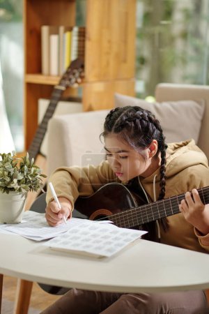 Foto de Chica arrancando la guitarra y escribiendo notas musicales - Imagen libre de derechos