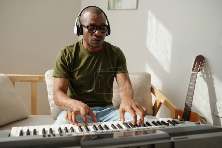 Téléchargez les photos : Musicien avec écouteurs jouant du piano électronique à la maison - en image libre de droit