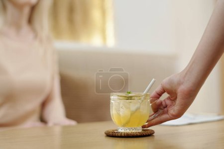 Téléchargez les photos : Réceptionniste mettant tasse avec thé glacé devant le client - en image libre de droit