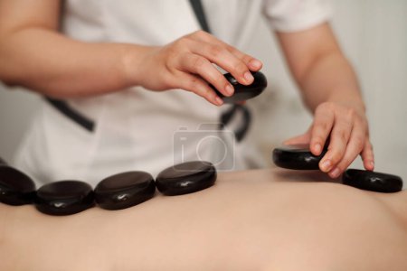 Photo for Hands of woman putting hot stones along spine of young woman - Royalty Free Image