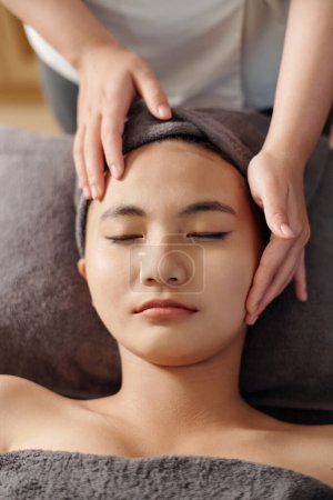 Téléchargez les photos : Cosmetoloigiste donnant au client un massage du visage anti-âge, vue d'en haut - en image libre de droit