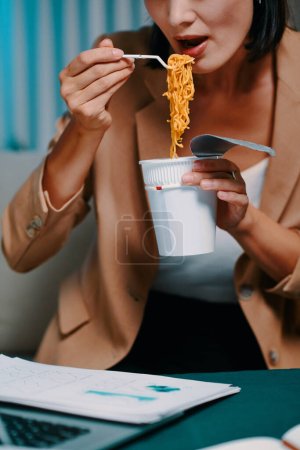 Photo for Cropped image of businesswoman eating instant noodles when working on report late at night - Royalty Free Image