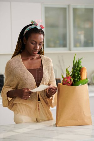 Photo for Black woman checking receipt after receviving food delivery - Royalty Free Image