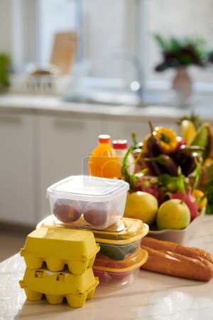 Foto de Recipientes con frutas y verduras frescas, huevos y pan en el mostrador de la cocina - Imagen libre de derechos