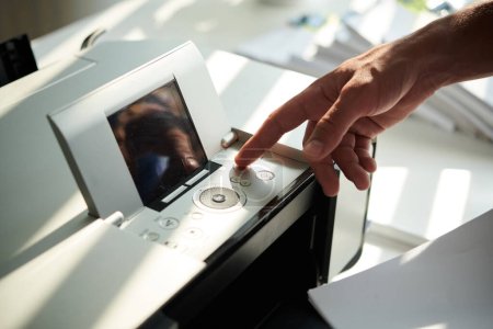 Téléchargez les photos : Homme d'affaires appuyant sur le bouton de l'imprimante pour imprimer des rapports pour réunion - en image libre de droit