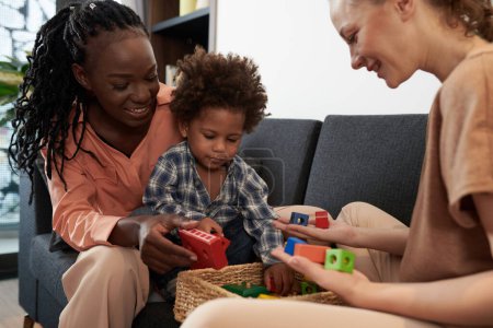 Téléchargez les photos : Joyeux mères montrant boîte de nouveaux jouets en bois colorés pour tout-petit fils - en image libre de droit