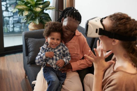 Photo for Smiling woman hugging little son when her girlfriend playing game in vr headset - Royalty Free Image