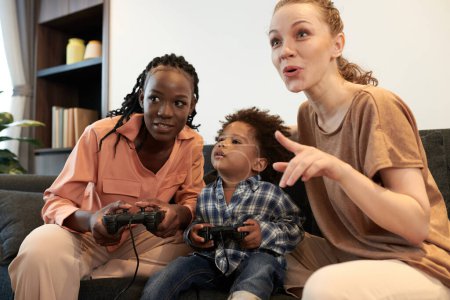Téléchargez les photos : Excité divers parents et tout-petit garçon jouer à un jeu vidéo ensemble à la maison - en image libre de droit